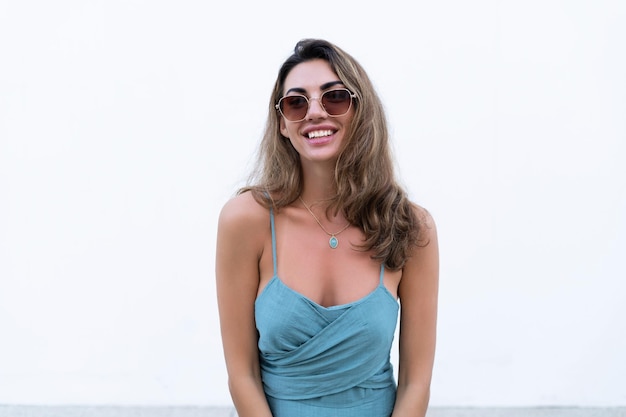 Portrait of beautiful woman in green fitting summer dress on white background natural day light wearing sunglasses smiling excited