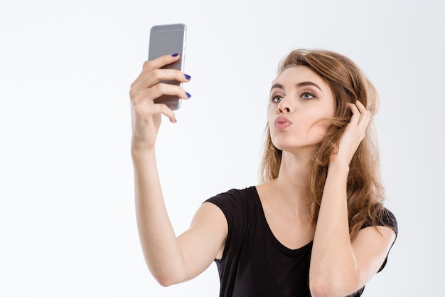 Portrait of a beautiful woman making selfie photo on smartphone isolated on a white background