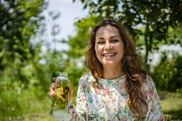 Portrait of beautiful woman posing lying on plaid at summer garden park a book fruit a bag and a wat