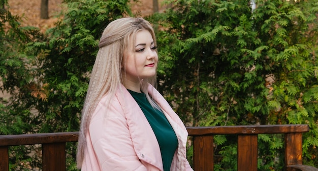 A portrait of a beautiful woman sitting on a bench near the green vegetation