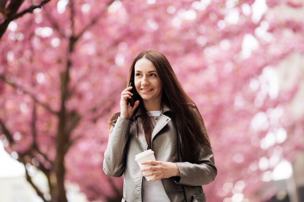 Portrait of a beautiful woman talking with her phone in Sakura tree park