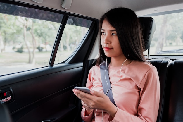 Portrait of beautiful woman using smart phone and thoughtfully looking out of the car.