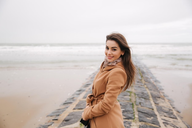 Portrait of beautiful woman walkink along the coast near the north sea Elegant lady in brown coat