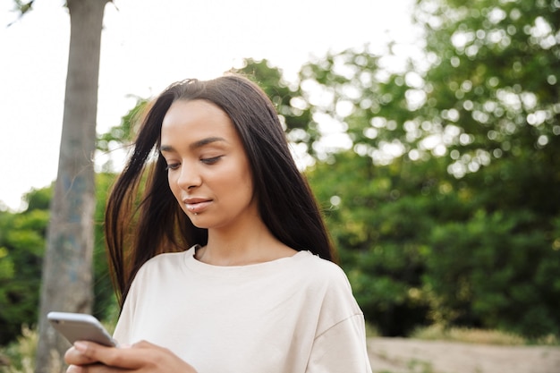 Portrait of beautiful woman wearing lip piercing holding smartphone while walking in green park