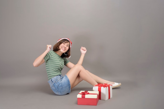 A portrait of beautiful woman wearing red Santa Claus hat holding gift box over studio background, Christmas and New Year Concept