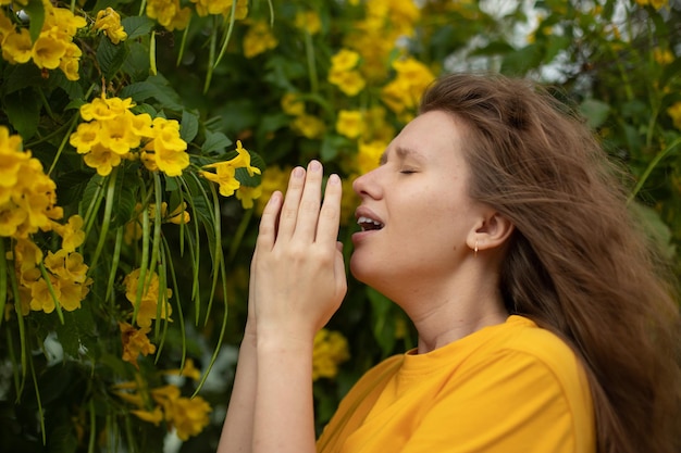 Portrait of beautiful young allergic woman is suffering from pollen allergy or cold on natural flower flowering tree background at spring or sunny summer day sneezes blowing her runny nose rubs eyes