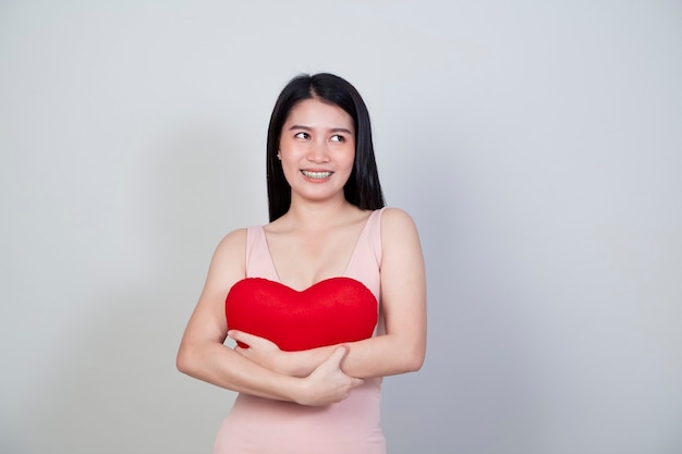 Portrait beautiful young Asian woman in dress show heart shape pillow isolated on light gray background with copy space