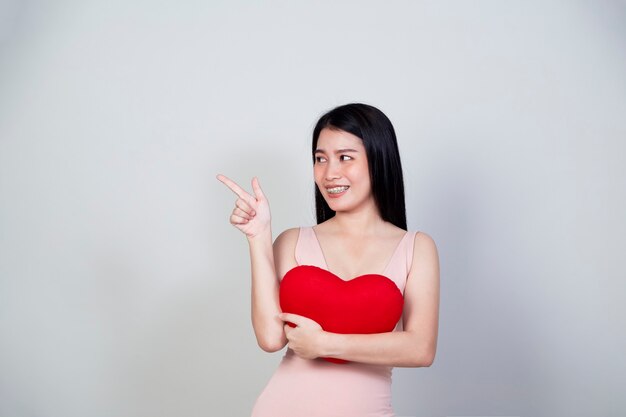 Portrait beautiful young Asian woman in dress show heart shape pillow isolated on light gray background with copy space