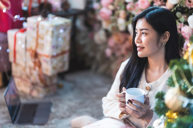 Portrait beautiful young asian woman girl wearing warm clothes enjoys drinking holding of positive the having cup of coffeemilk or chocolate and laptop at house home in the living room inside or cafe