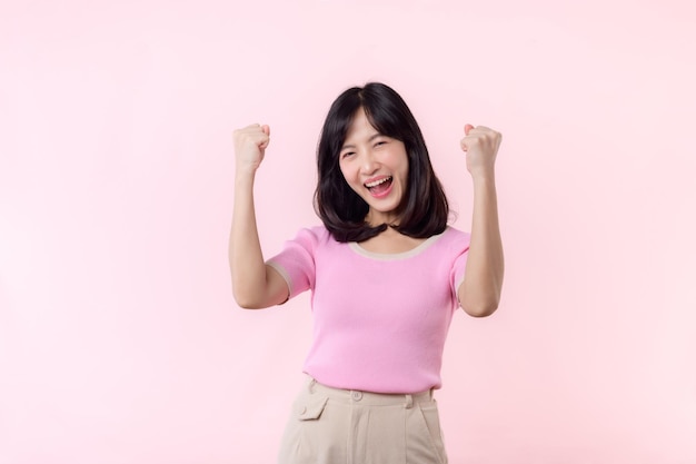 Portrait beautiful young asian woman happy smile with fist up victory gesture expression cheerful her success achievement against pink pastel studio background Woman day winner celebration concept