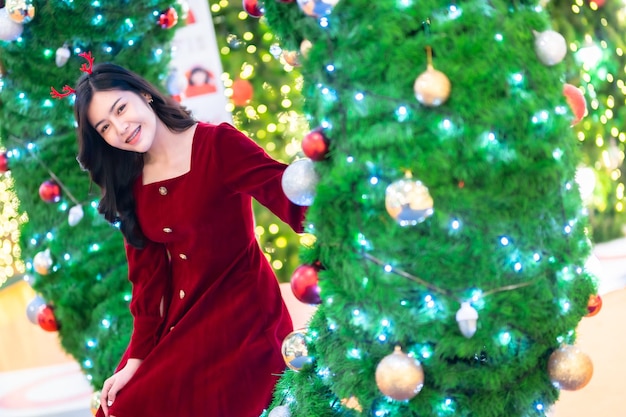 Portrait beautiful young asian woman red dress costume and Christmas greeting picture parcel decoration on Christmas tree light circular bokeh background Decoration During Christmas and New Year.