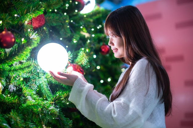 Portrait beautiful young asian woman red dress costume and Christmas greeting picture parcel decoration on Christmas tree light circular bokeh background Decoration During Christmas and New Year