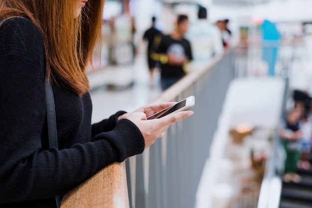 Portrait of beautiful young asian woman in shopping mall, smiling using smart phone