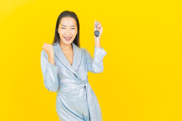 Portrait beautiful young asian woman smile with car key on yellow wall