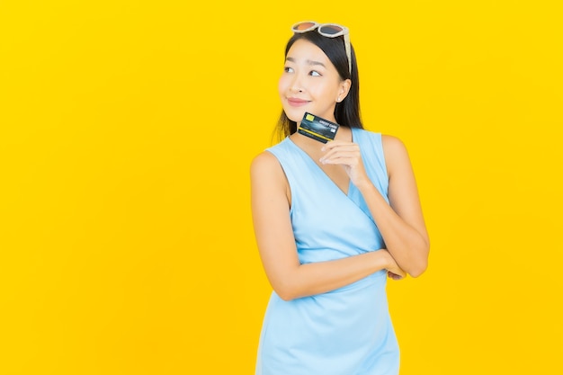 Portrait beautiful young asian woman smile with credit card on yellow color wall