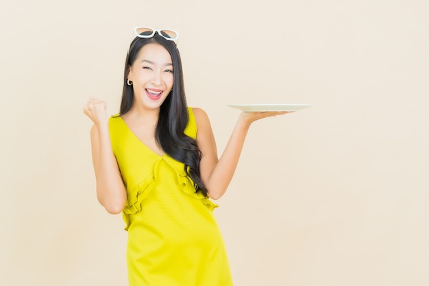 Portrait beautiful young asian woman smile with empty plate dish on color wall