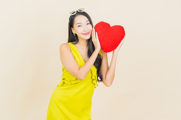 Portrait beautiful young asian woman smile with heart pillow shape on color wall