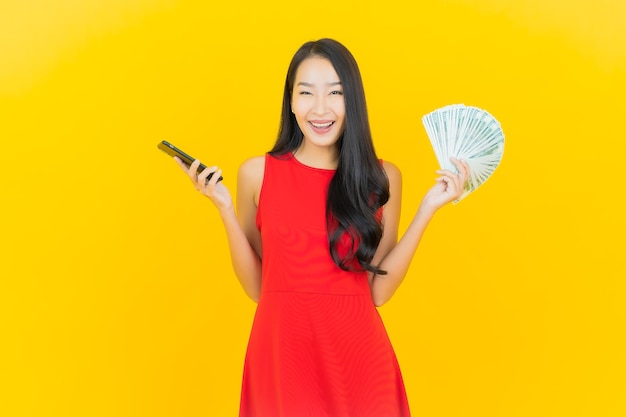 Portrait beautiful young asian woman smile with a lot of cash and money on yellow wall