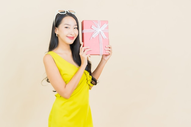 Portrait beautiful young asian woman smile with red gift box on color wall