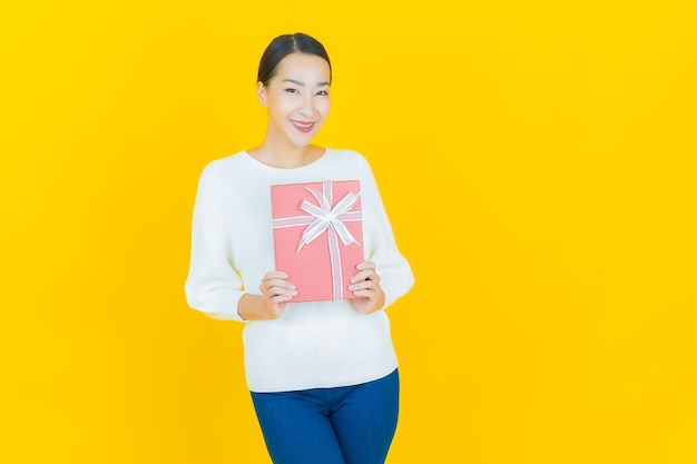 Portrait beautiful young asian woman smile with red gift box on yellow