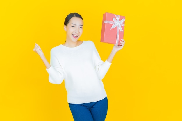 Portrait beautiful young asian woman smile with red gift box on yellow