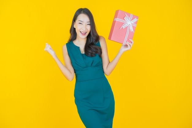 Portrait beautiful young asian woman smile with red gift box on yellow