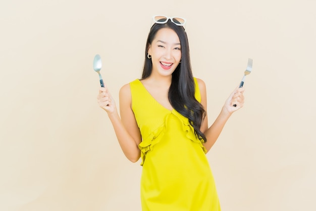 Portrait beautiful young asian woman smile with spoon and fork on color wall