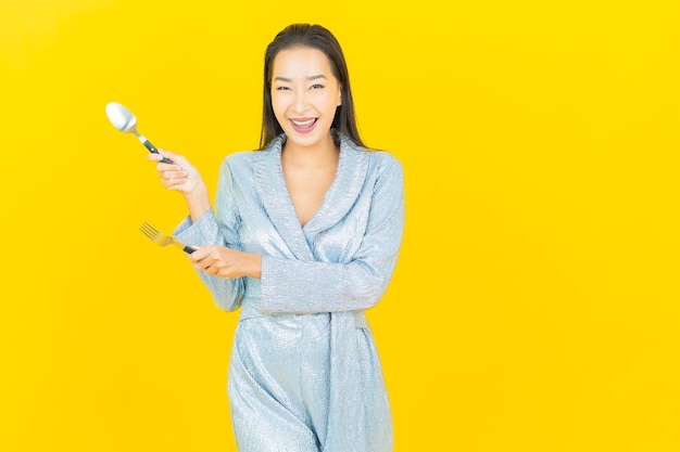 Portrait beautiful young asian woman smile with spoon and fork on yellow wall