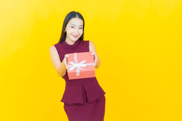 Portrait beautiful young asian woman smiles with red gift box on yellow wall