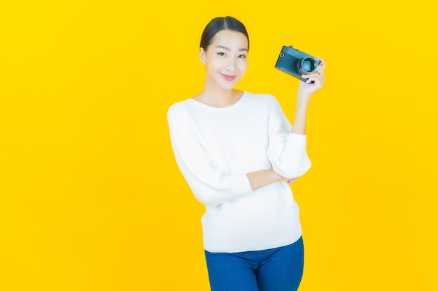 Portrait beautiful young asian woman use camera on yellow