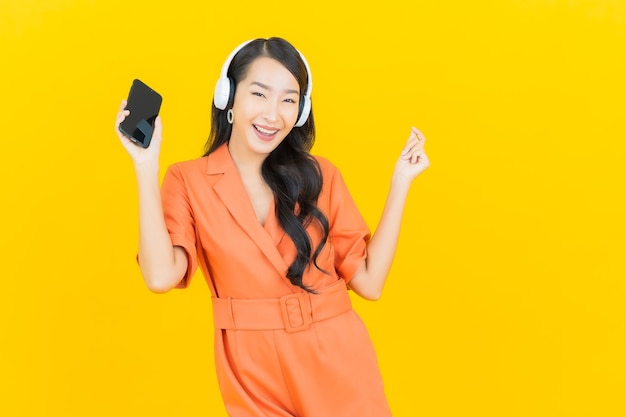 Portrait beautiful young asian woman with headset and smart mobile phone listen to music on yellow