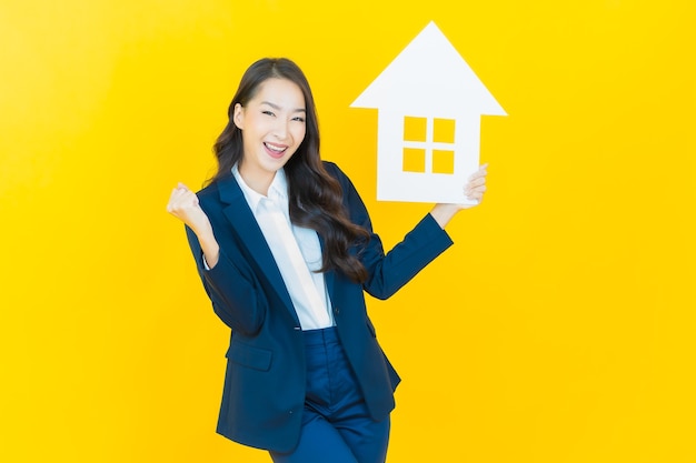 Portrait beautiful young asian woman with house or home paper sign on yellow