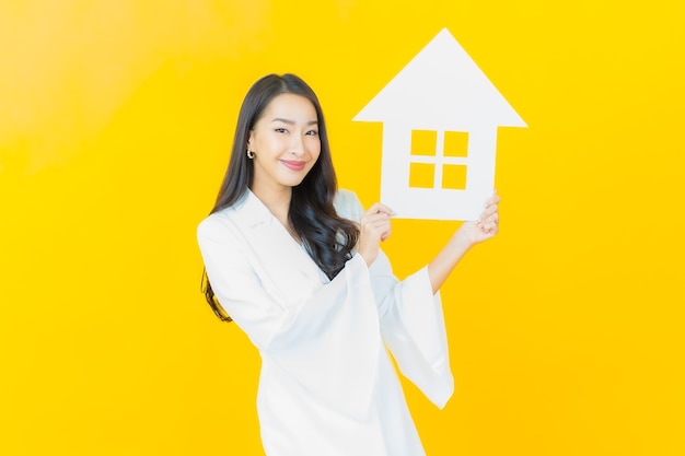 Portrait of beautiful young asian woman with paper house on yellow wall