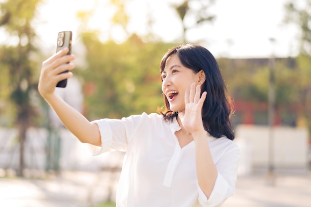 Portrait beautiful young asian woman with smart mobile phone around outdoor nature view in a sunny summer day