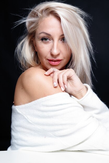 Photo portrait of a beautiful young attractive woman in a white sweater with blue eyes and long blond hair.