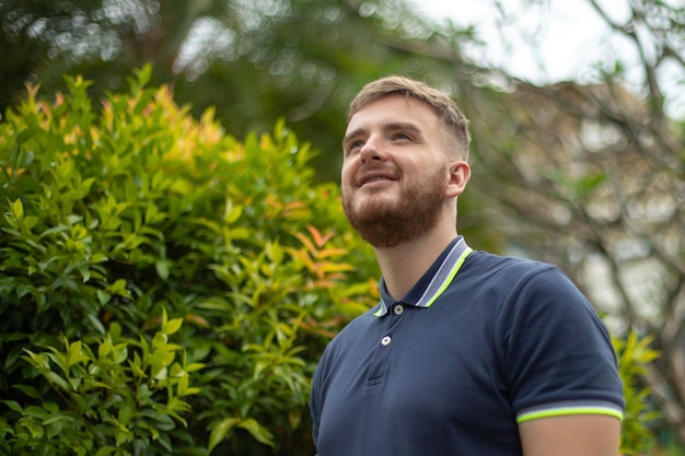 Portrait of a beautiful young bearded man with beard standing on an Ivy wall or in greenery smiling against from plant guy relaxing outdoors at sunny summer day Love nature eco life