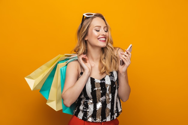 Portrait of a beautiful young blonde woman standing isolated over yellow background, using mobile phone