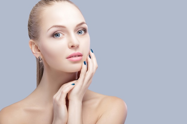 portrait of beautiful young blonde woman with blue eyes on grey background closeup.  Woman Touching her Face