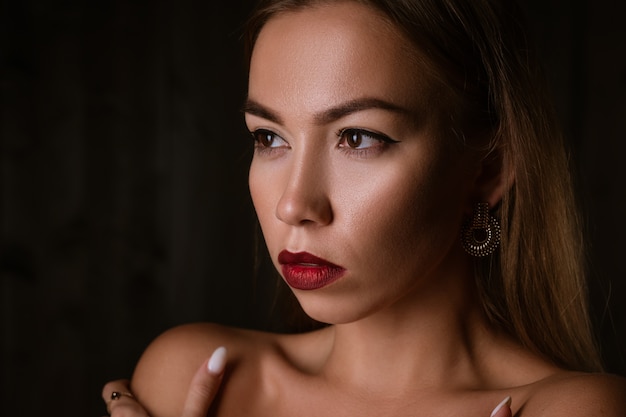 Portrait of a beautiful young brunette girl with painted lips and an earring on a black background