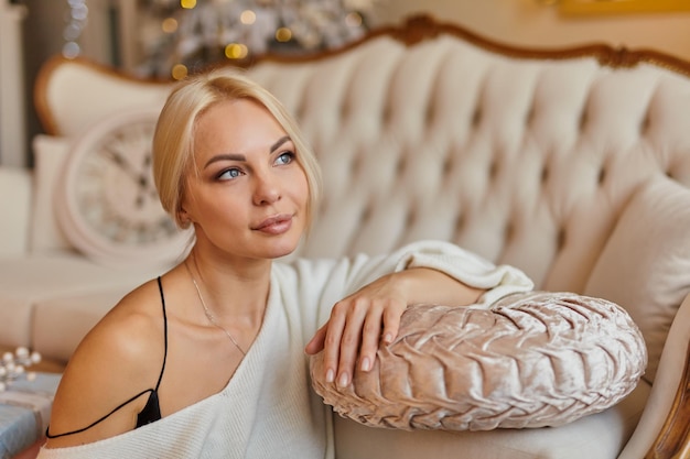 Portrait of Beautiful young elegant woman at home sitting with his elbows on the sofa with a cup of tea and thinks about plans for next year. warm, cozy, festive, christmas environment