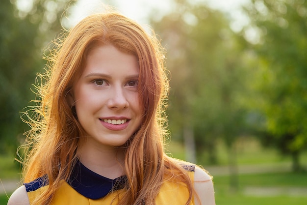 Portrait of beautiful young ginger redhead irish woman in a yellow dress stylish makeup and fresh toothy smile in the summer park concept of girlish freshness and femininity