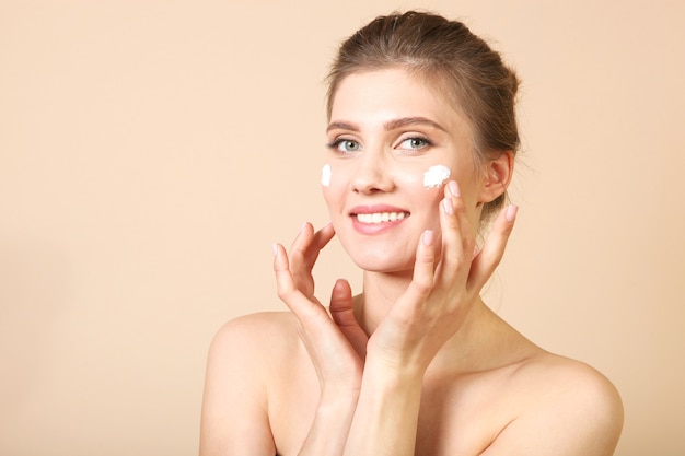 Portrait of a beautiful young girl on a colored background who uses caring cream