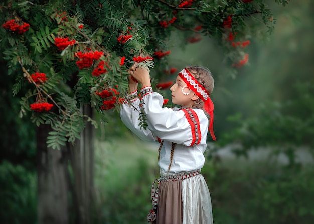 Portrait of a beautiful young girl in folk dress near a Rowan tree