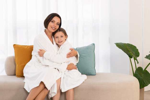 Portrait of beautiful young mom and little daughter posing in white bathrobes