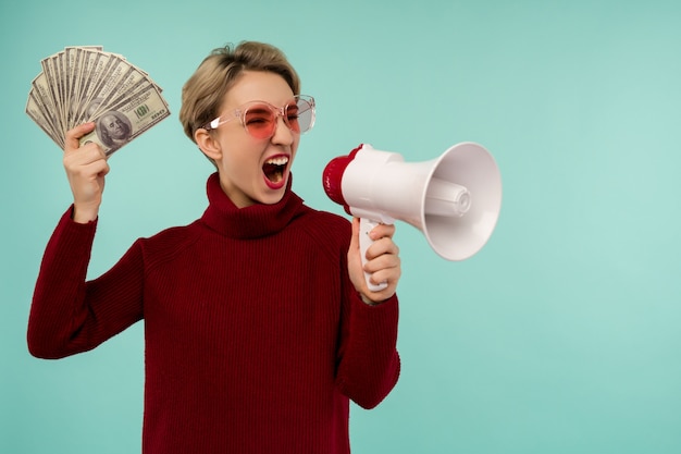 Portrait of beautiful young screaming woman with money and megaphone,