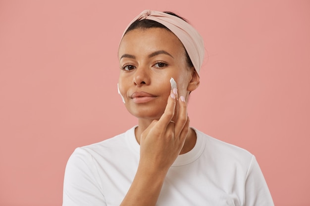 Portrait of beautiful young woman applying face cream