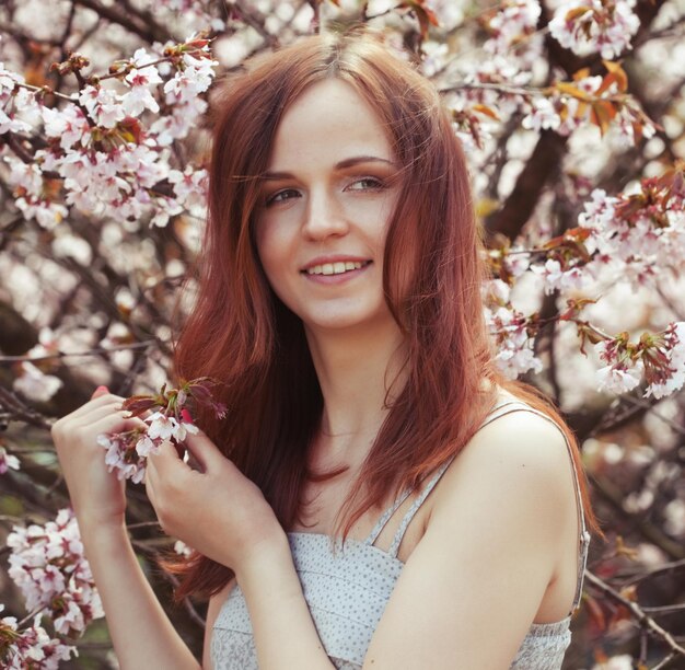 Portrait of a beautiful young woman on a background of pink cherry blossoms in spring