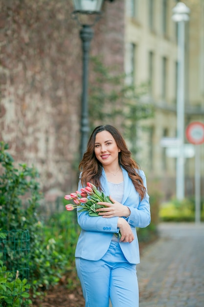 Portrait of a beautiful young woman in a blue suit with a bouquet of tulips