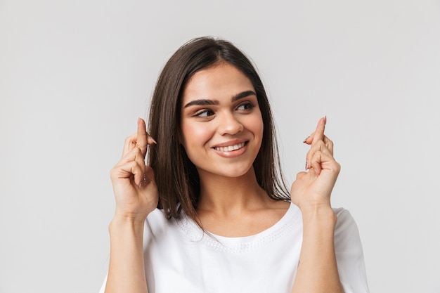 Portrait of a beautiful young woman casualy dressed standing isolated on white, holding fingers crossed for good luck