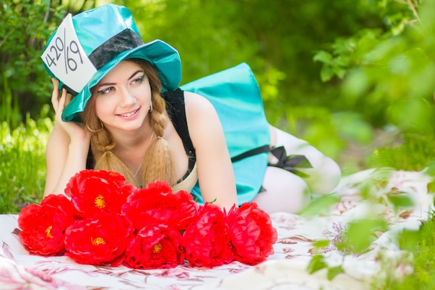 Portrait of a beautiful young woman in a costume of the Mad Hatter in nature. woman posing with a bouquet of red peonies